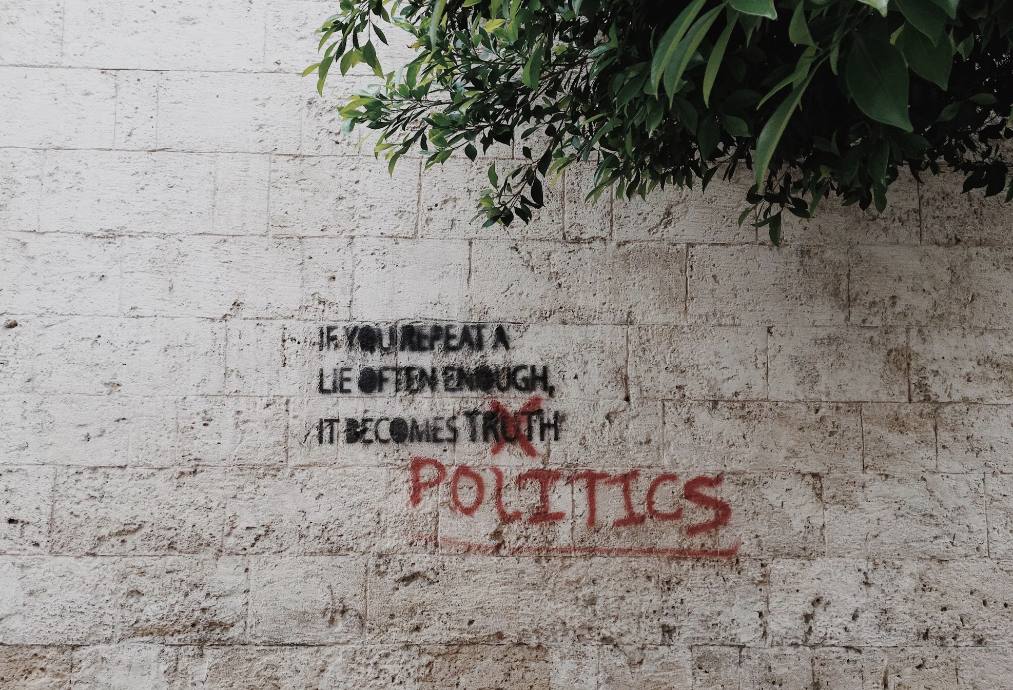 Grafitti en inglés cuya traducción es: "Si repites una mentira lo suficiente, se convierte en realidad" la palabra realidad se encuentra tachada en rojo y en rojo también escriben "política"